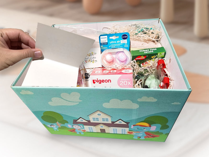 A hand placing a message card into a packed Happy Kind Kiddo gift box